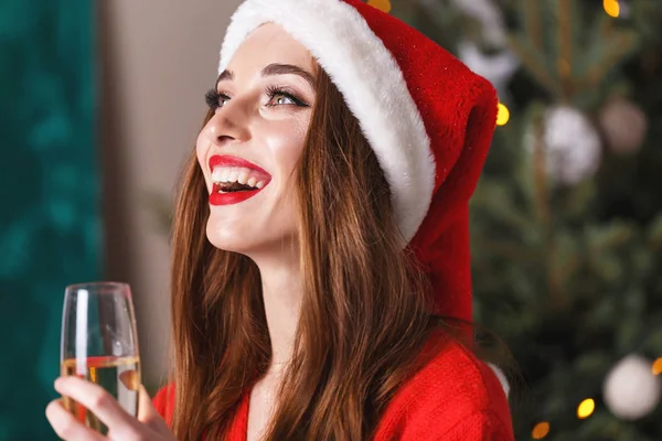 Hermosa mujer de Navidad con sombrero de Santa bebiendo champán mientras se hospeda cerca del abeto de año nuevo — Foto de Stock