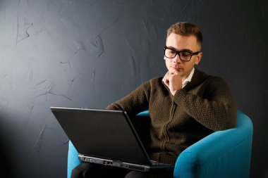 Turkuaz koltukta oturan ve laptop ile çalışan yeşil kazak giyen ciddi yakışıklı genç