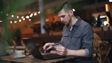 O dizüstü ve kafe iç otururken bir şey satın almak onun kartı numaralarını yazarak onun kredi kartı ile alışveriş rahat kıyafet sahip giyen adam