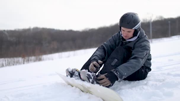 Mann verriegelt Stiefel auf Snowboard zum Skifahren — Stockvideo