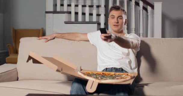 Возбужденный человек смотрит телевизор и ест пиццу — стоковое видео