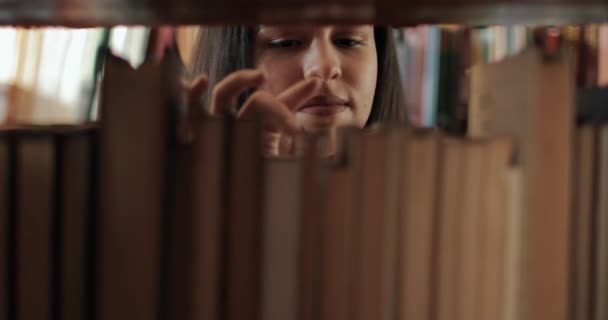 Menina busca livro na biblioteca — Vídeo de Stock