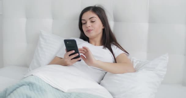 Gadis cantik menggunakan Smartphone di tempat tidur — Stok Video