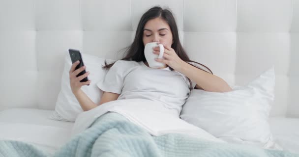 Chica usando el teléfono y tener café en la cama — Vídeos de Stock
