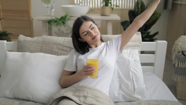 Fröhliches Mädchen trinkt Orangensaft im Bett — Stockvideo