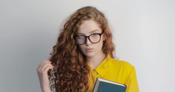 Estudiante joven con cabello rizado posando con libro y gafas — Vídeos de Stock