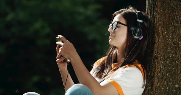 Kvinna i hörlurar lyssnar på musik i parken — Stockvideo