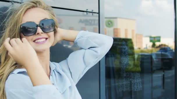 Vrouw in zonnebril staande in de buurt van muur wind — Stockvideo