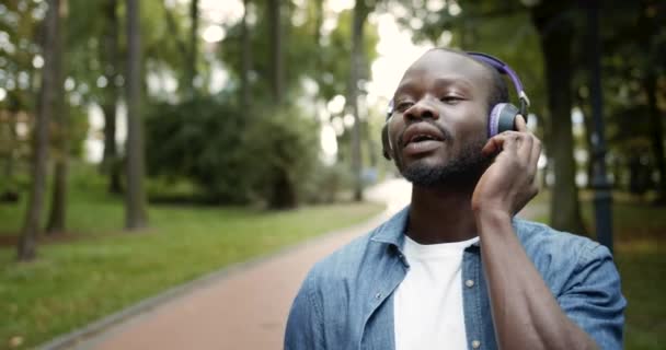 Afroamerikaner mit Kopfhörern singt im Park — Stockvideo