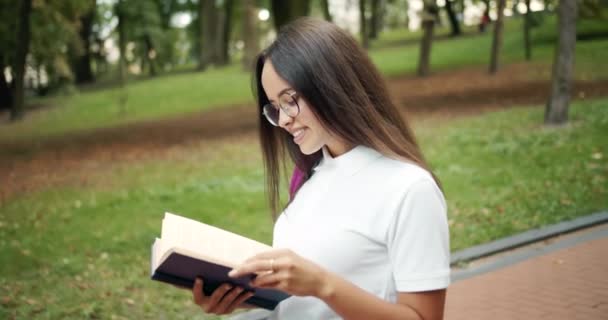 Estudiante caminando y leyendo libro en el parque — Vídeos de Stock
