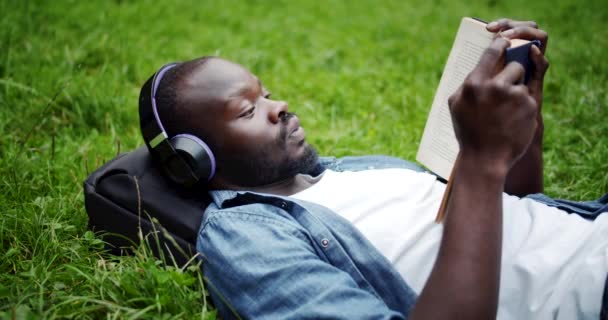 Afrikanisch-amerikanischer Mann liegt mit Buch auf Rasen — Stockvideo