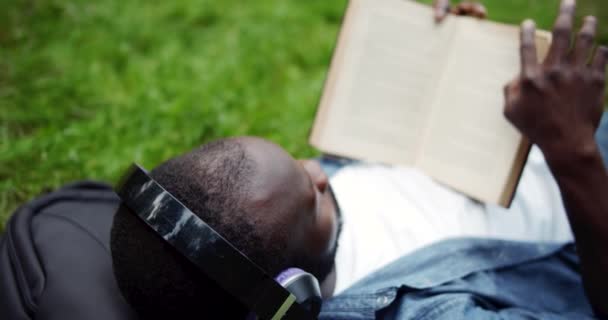 Hombre afroamericano acostado en el césped con libro — Vídeo de stock