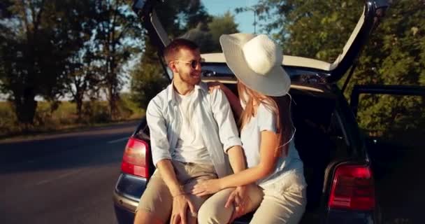 Pareja sentada en el maletero del coche al atardecer — Vídeos de Stock