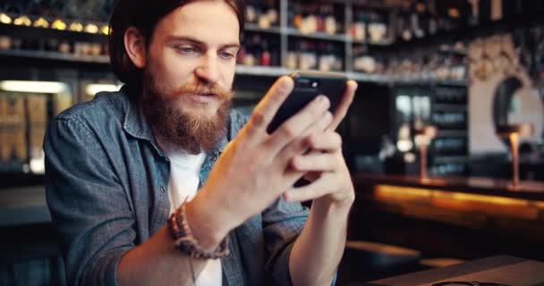 Vousatý muž se smartphone v kavárně — Stock video