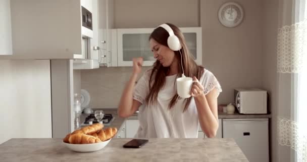 Vrouw in hoofdtelefoon in keuken ochtend — Stockvideo