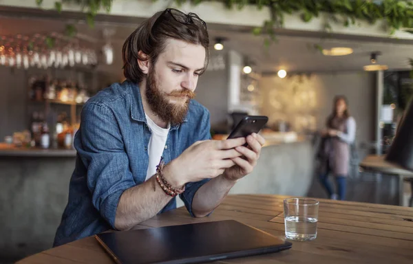 Brązowłosy młody człowiek za pomocą smartfona w Loft Cafe — Zdjęcie stockowe