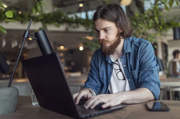 Hombre joven trabajando por ordenador portátil en un Loft Café —  Fotos de Stock