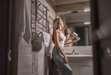 Saç kurutma makinesi kullanan sevimli genç kız.