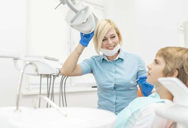Sorrindo Loira Dentista Feminina Ajustando a Lâmpada Refletora Dental — Fotografia de Stock
