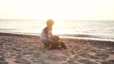 Sahilde çikolata labrador ile gündoğumu ışıkta oynarken erkek