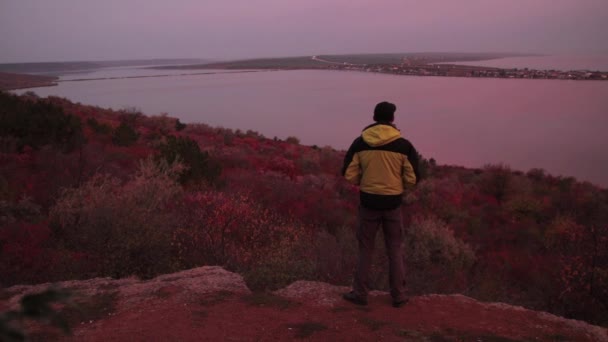 男子徒步者站在边缘 欣赏湖面上的香草日出 道路的灯光 — 图库视频影像