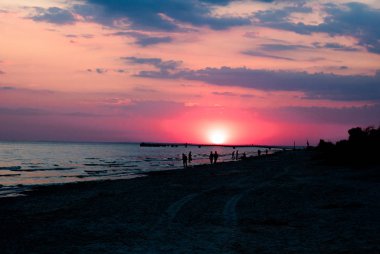 Sahilde kırmızı günbatımı. İnsanlar siluetleri ve martı sahilde. İskelede manzarası