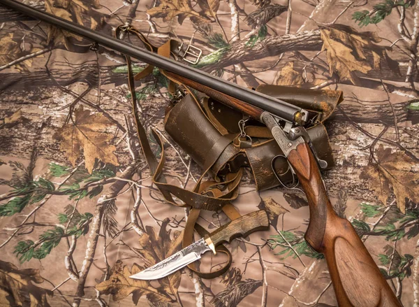antique double-barreled shotgun, knife and ammunition belt on the camouflage background