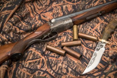 antique double-barreled shotgun, knife and ammunition belt on the camouflage background clipart
