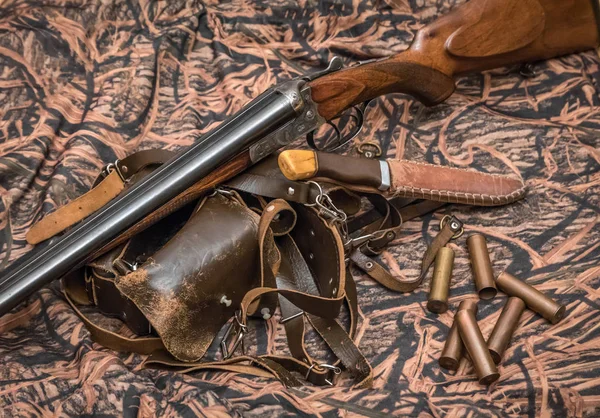 antique double-barreled shotgun, knife and ammunition belt on the camouflage background