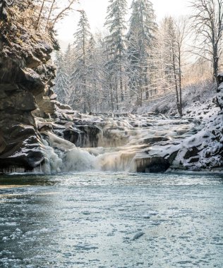 Buharlama taşlar, turuncu güneş ışığı, donmuş gölet arasında buzlu kış şelale