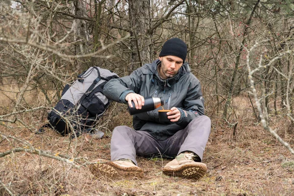 hiker man resting in the forest and drinking tea from the thermos