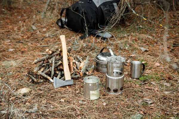 axe near a firewoods, camping woodstove, camping utensils and backpack on the background