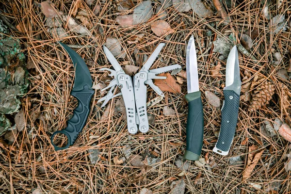 Туристический нож, карамбит, многоинструментарий и ножик на земле, покрытый сосновыми иглами — стоковое фото