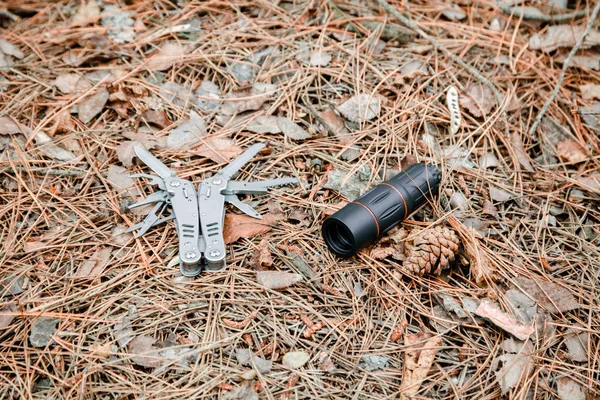 Монокль и многоинструментальный нож на земле, покрытый сосновыми иглами — стоковое фото