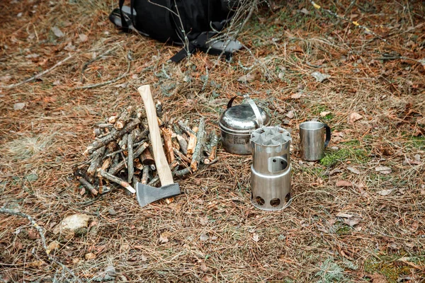 axe near a firewoods, camping woodstove, camping utensils and backpack on the background