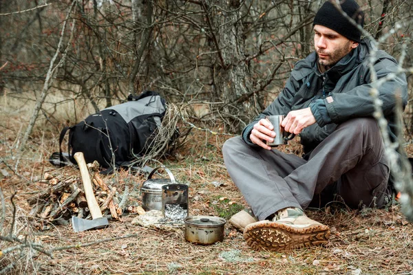 man relaxing in the forest camping, near the wood stove, utensils and axe with firewoods