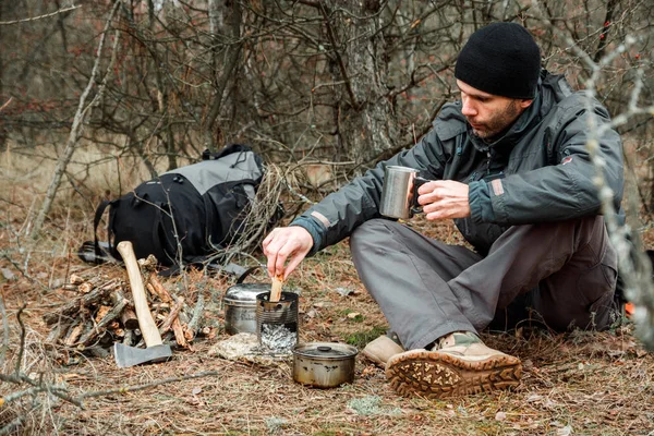 Ο άνθρωπος χαλαρώνοντας στο camping δάσος, κοντά στην σόμπα ξύλου, σκεύη και τσεκούρι με καυσόξυλα — Φωτογραφία Αρχείου