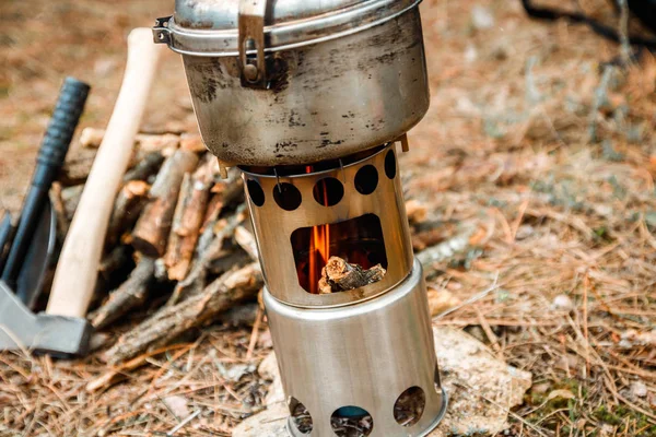 camping woodstove and utensils, axe and sapper shovel near a firewoods, and backpack on the background