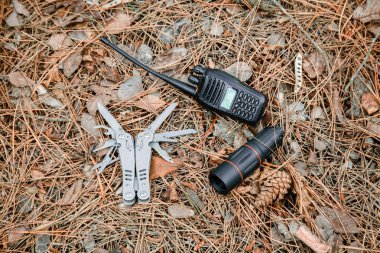 monokl, radyo seti ve multitool bıçağı yere çam iğneleri ile kaplı