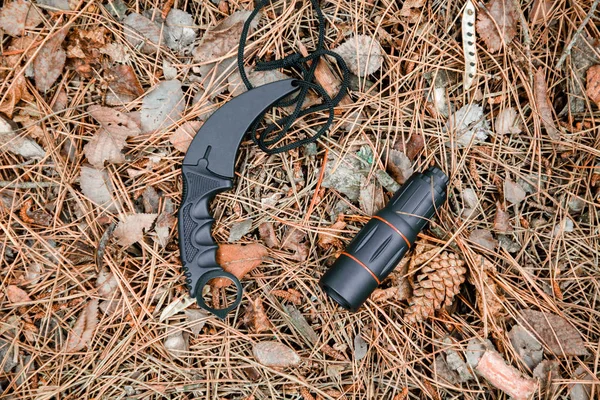 Monocle and karambit knife on the ground covered with pine needles — Stock Photo, Image