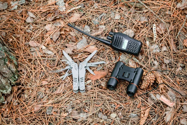 Binocolo, radio set e coltello multitool a terra ricoperto da aghi di pino — Foto Stock