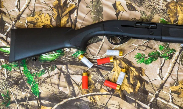 Escopeta negra de calibre 12 y cartuchos sobre fondo de camuflaje — Foto de Stock