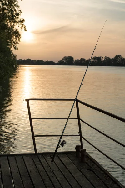 Orange solnedgång genom molnen på floden. fiskespö på planka kaj — Stockfoto