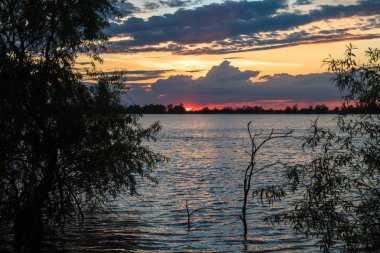 nehir tuna üzerinde güzel bulutlar ve turuncu gökyüzü ile doğal mavi ve kırmızı gün batımı
