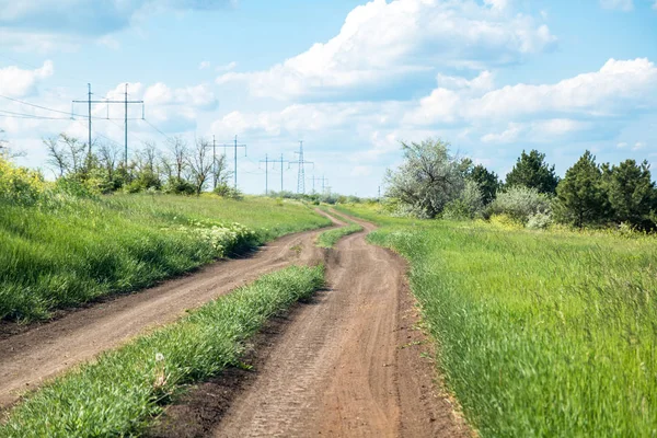 Route rurale entre champ et petite forêt, ciel bleu avec nuages — Photo