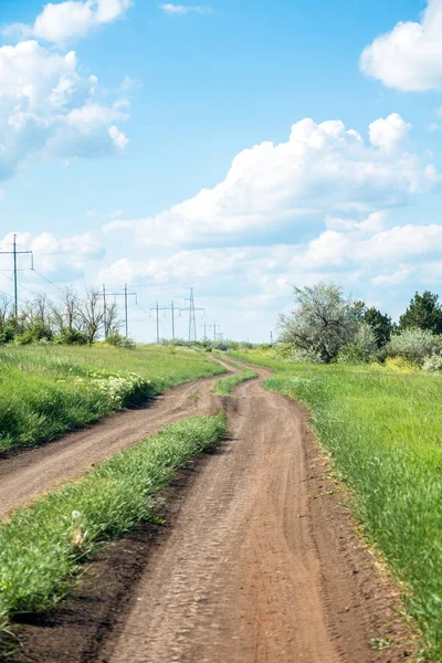 Route rurale entre champ et petite forêt, ciel bleu avec nuages — Photo