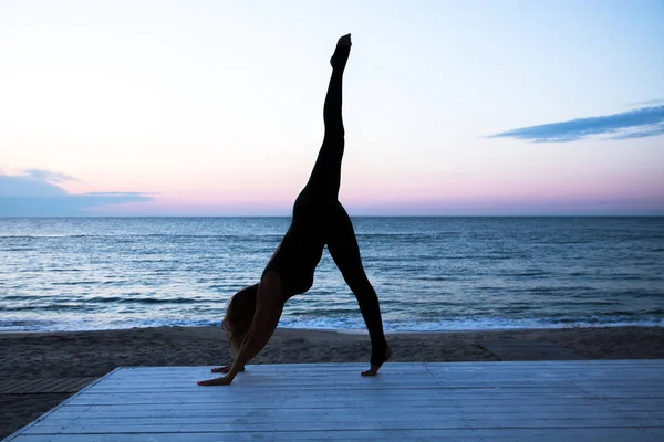Женщина делает йогу на восходе солнца на море, силуэт йоги позы — стоковое фото