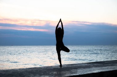 denizde gün doğumunda yoga yapan güzel vücut ile tanınmaz senoir kadın, yoga silueti pozlar
