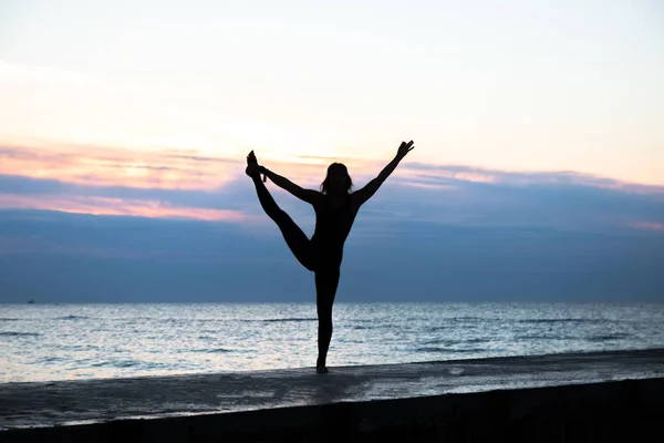 unrecognizable senoir woman with beautiful body doing yoga at sunrise on the sea, silhouette of yoga poses