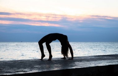 denizde gün doğumunda yoga yapan güzel vücut ile tanınmaz senoir kadın, yoga silueti pozlar